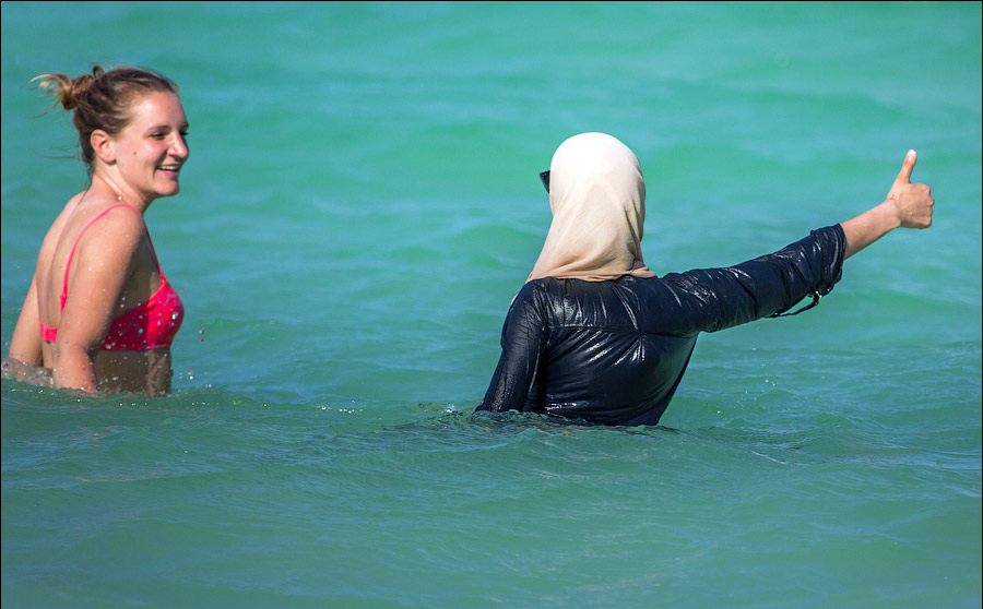 Две женщины в море. Одна женщина в купальнике, другая одета в мусульманское одеяние. Наши женщины в Турции
