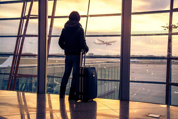 Пассажир с чемоданом смотрит с терминала на рулежную дорожку аэропорта