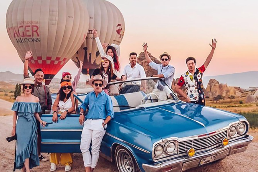 Компания друзей на раритетном авто фотографируются напротив воздушных шаров в Каппадокии, Турция