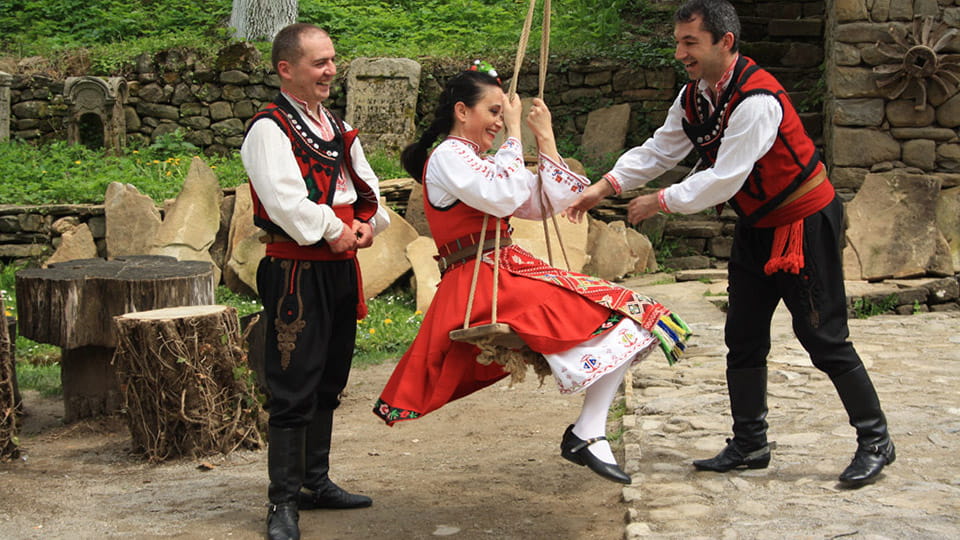 Двое мужчин и женщина в национальной одежде на Георгиев день в Болгарии