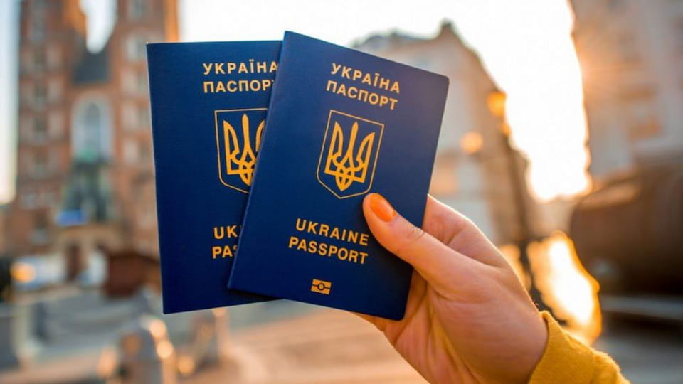 Два украинских биометрических загранпаспорта в руке туриста на фоне домов